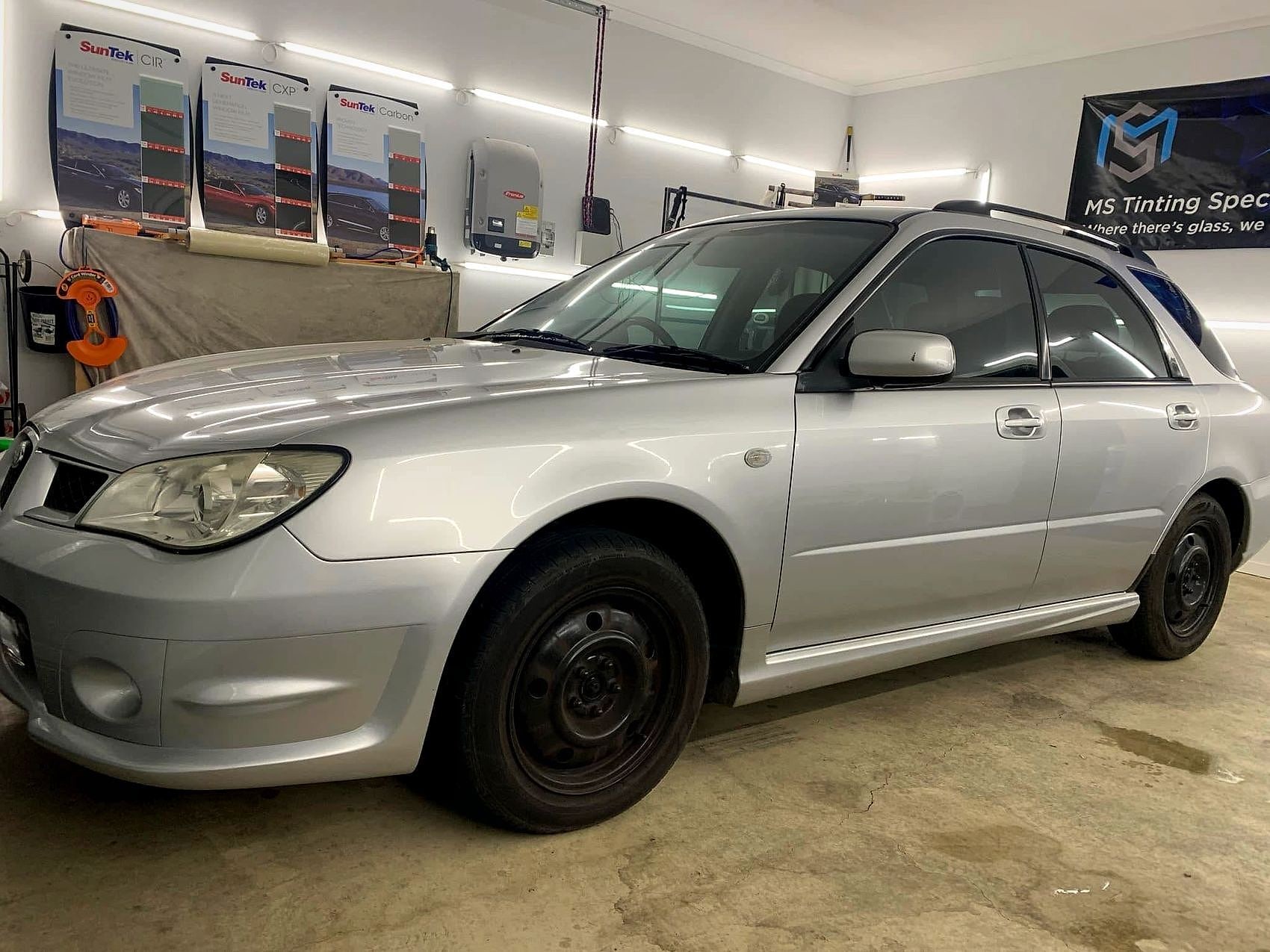 A silver Subaru tinted in the MS Tinting Specialist workshop next to SunTek film samples